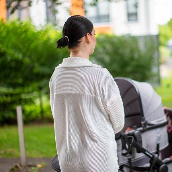 Eine junge Frau steht vor einem Kinderwagen.