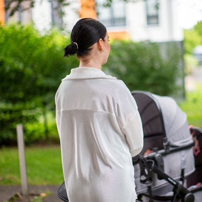 Eine junge Frau steht vor einem Kinderwagen.
