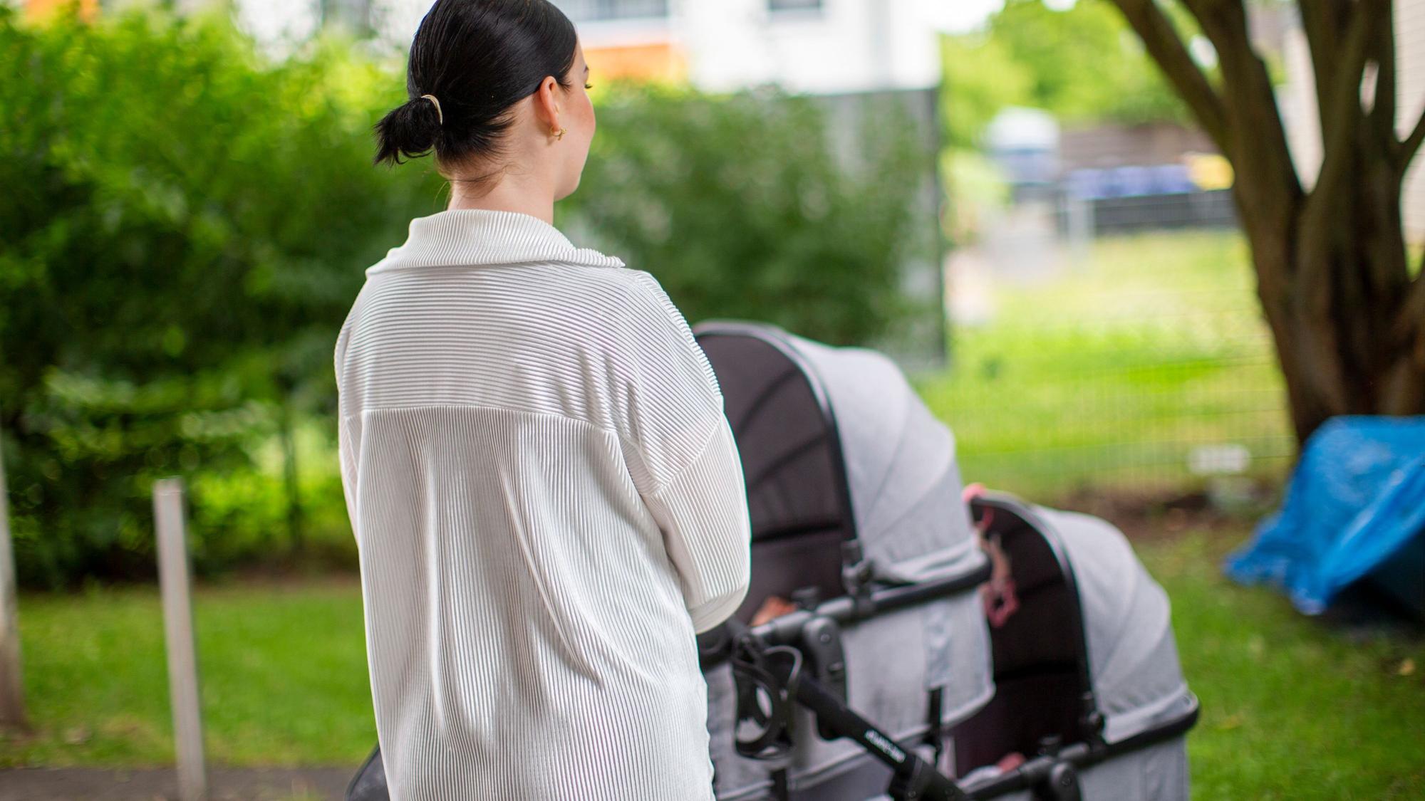 Eine junge Frau steht vor einem Kinderwagen.