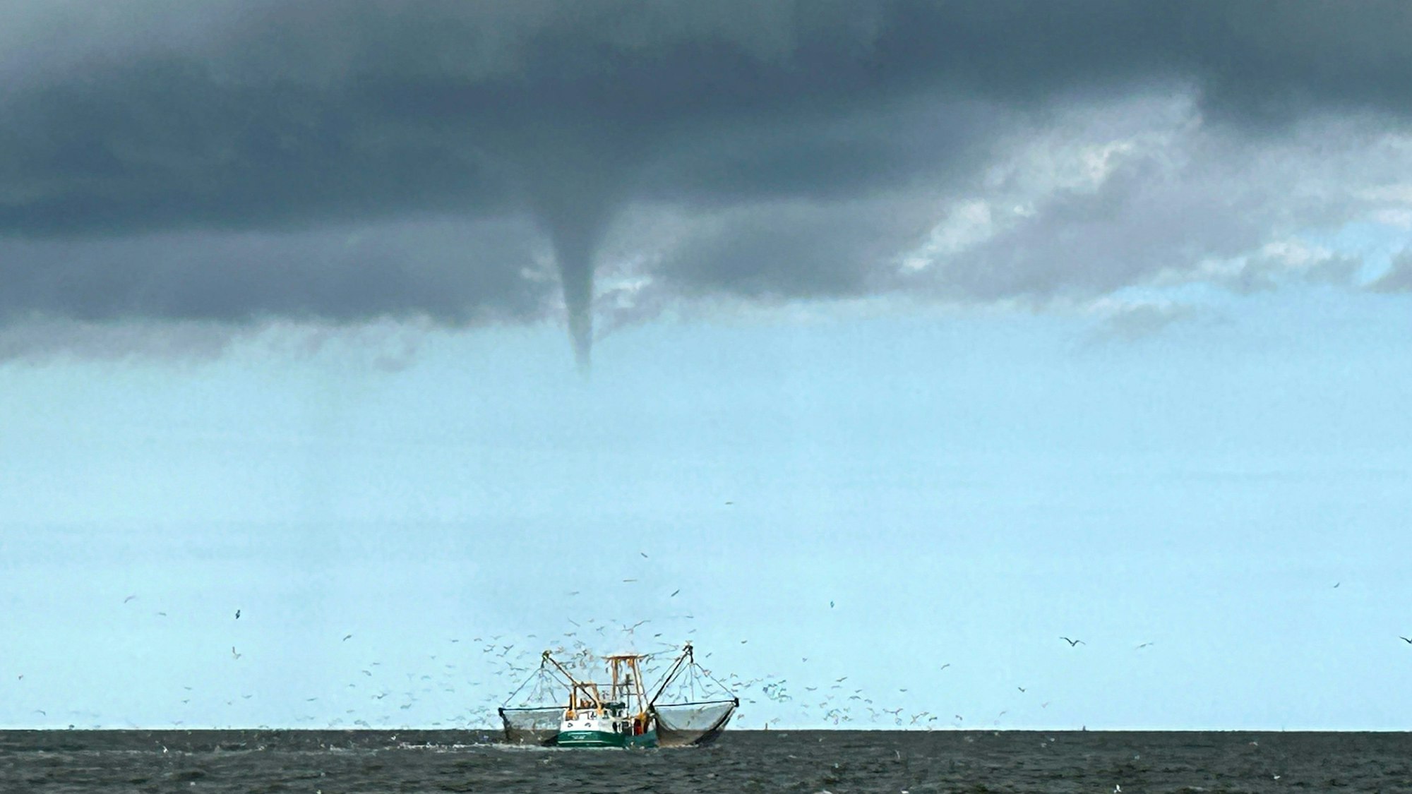 08.08.2024, Niedersachsen, Borkum: Das von einem Fischerboot aufgenommene Foto zeigt einen entstehenden mutmaßlichen Tornado vor der Nordseeinsel Borkum und ein Fischerboot.