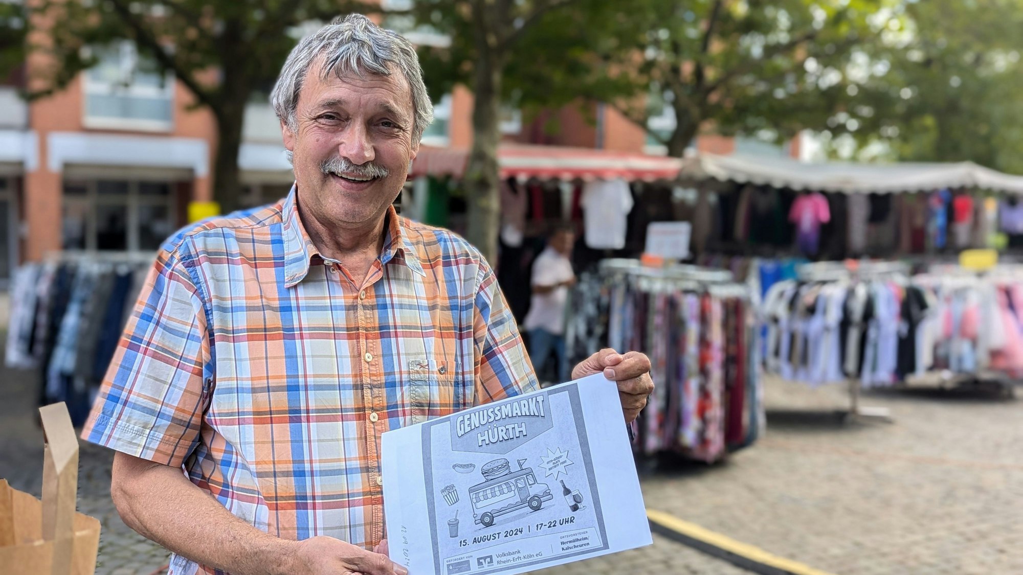 Marktmeister Hans-Josef Lang mit einem Entwurf für den Flyer zum Genussmarkt vor den Ständen des Wochenmarkts.