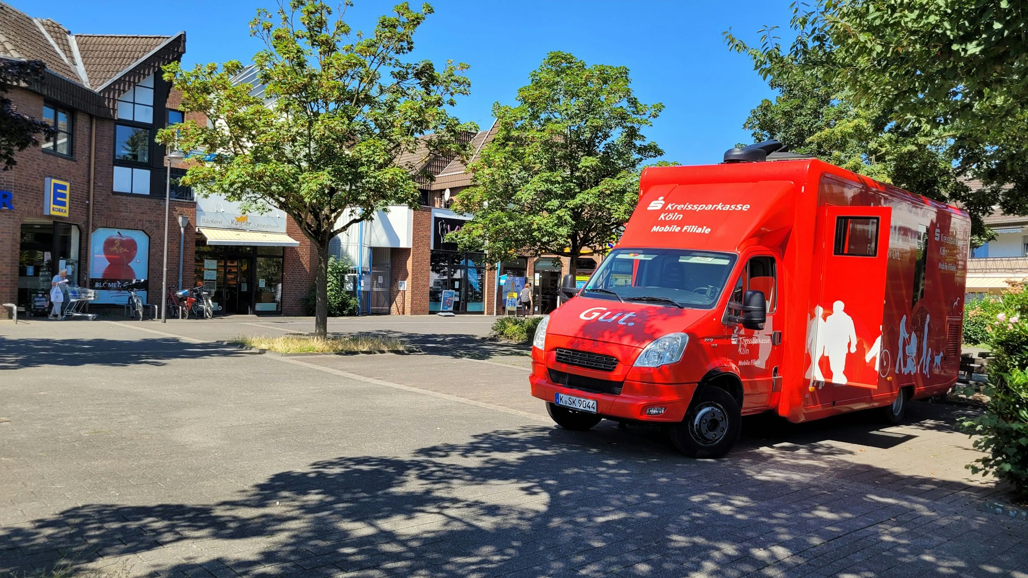 Ein Dorfplatz, rechts ein Mobil der Kreissparkasse.