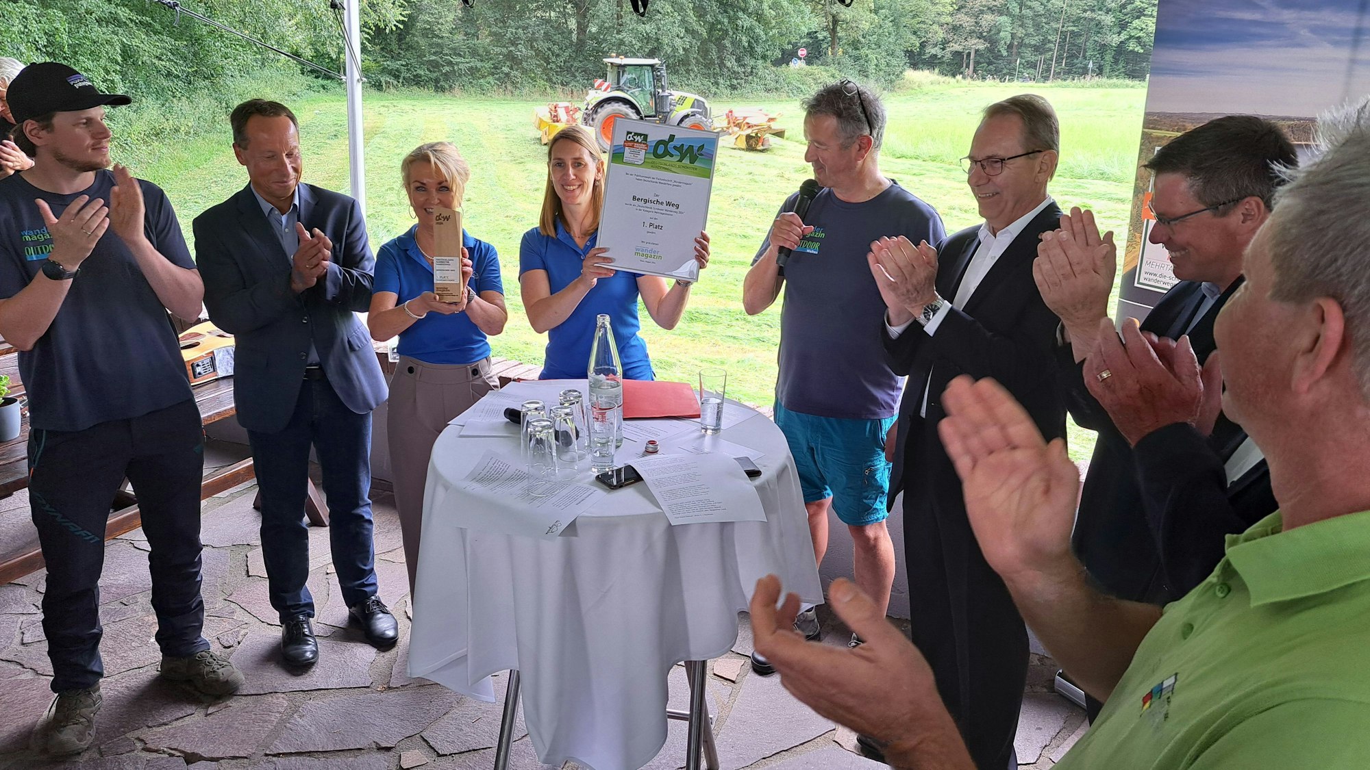 Eine Frau hält eine Urkunde in die Höhe, die Umstehenden klatschen.