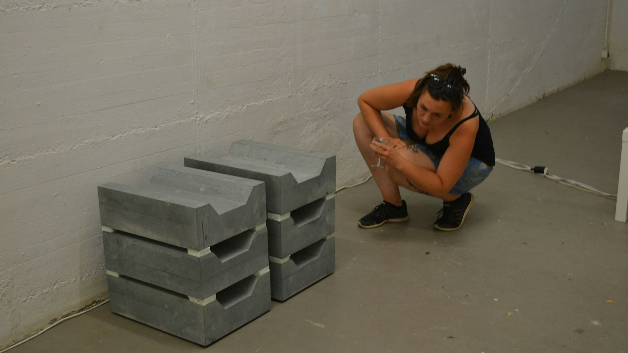 Eine Frau in der Hocke vor aufeinandergestapelten grauen Blöcken.