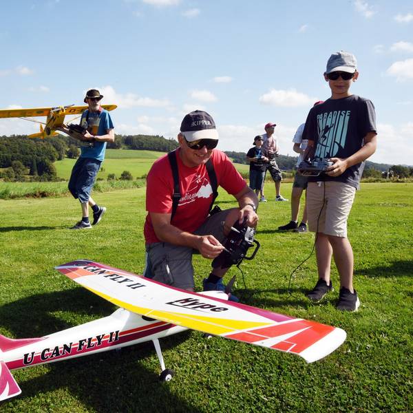 Ein Mann hockt neben einem Modellflugzeug. Er hält eine Fernbedienung in der Hand. Neben ihm steht ein Junge.