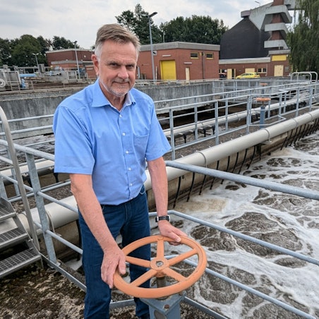 Ein Mann im kurzärmeligen Hemd an einem Schieber vor dem sprudelndem Wasser im Klärbecken.