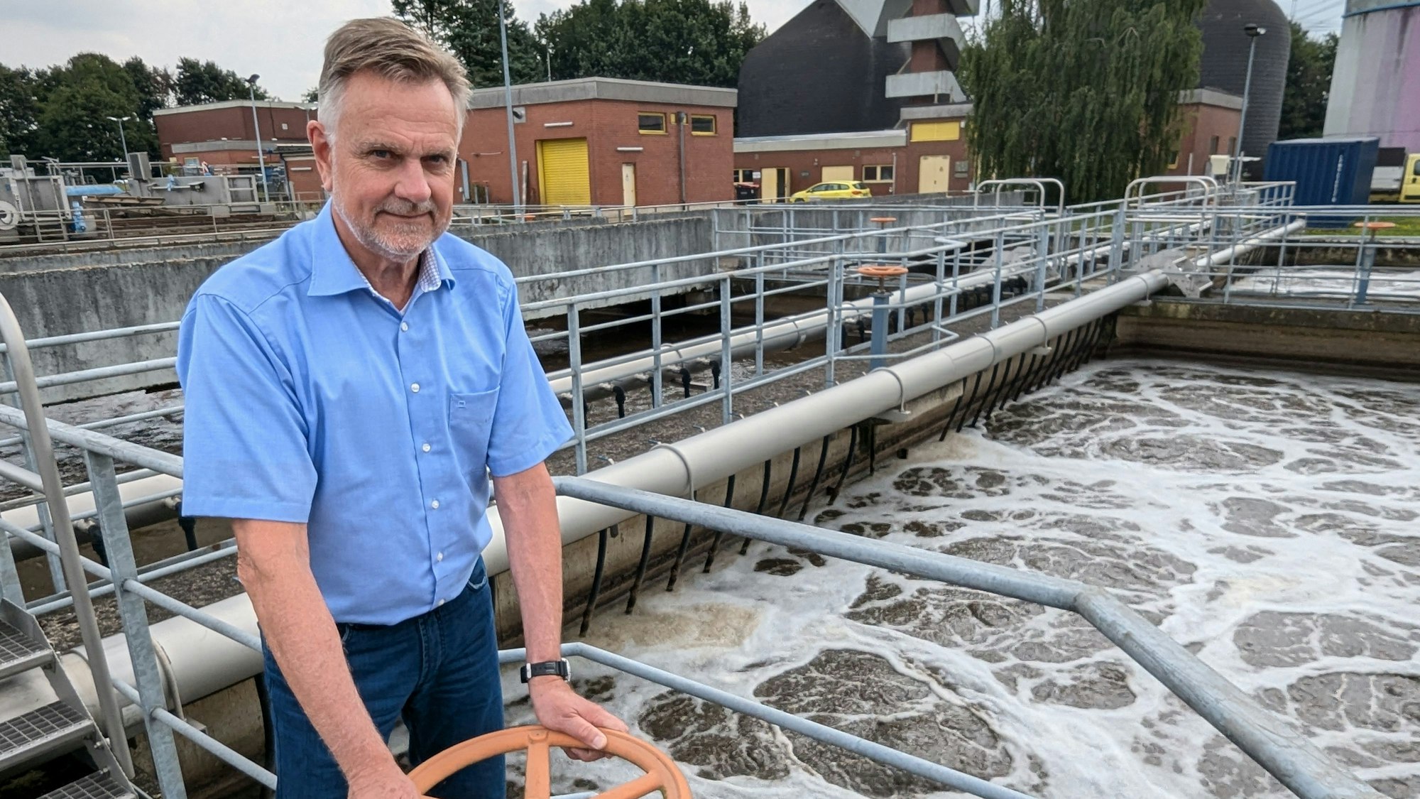 Ein Mann im kurzärmeligen Hemd an einem Schieber vor dem sprudelndem Wasser im Klärbecken.