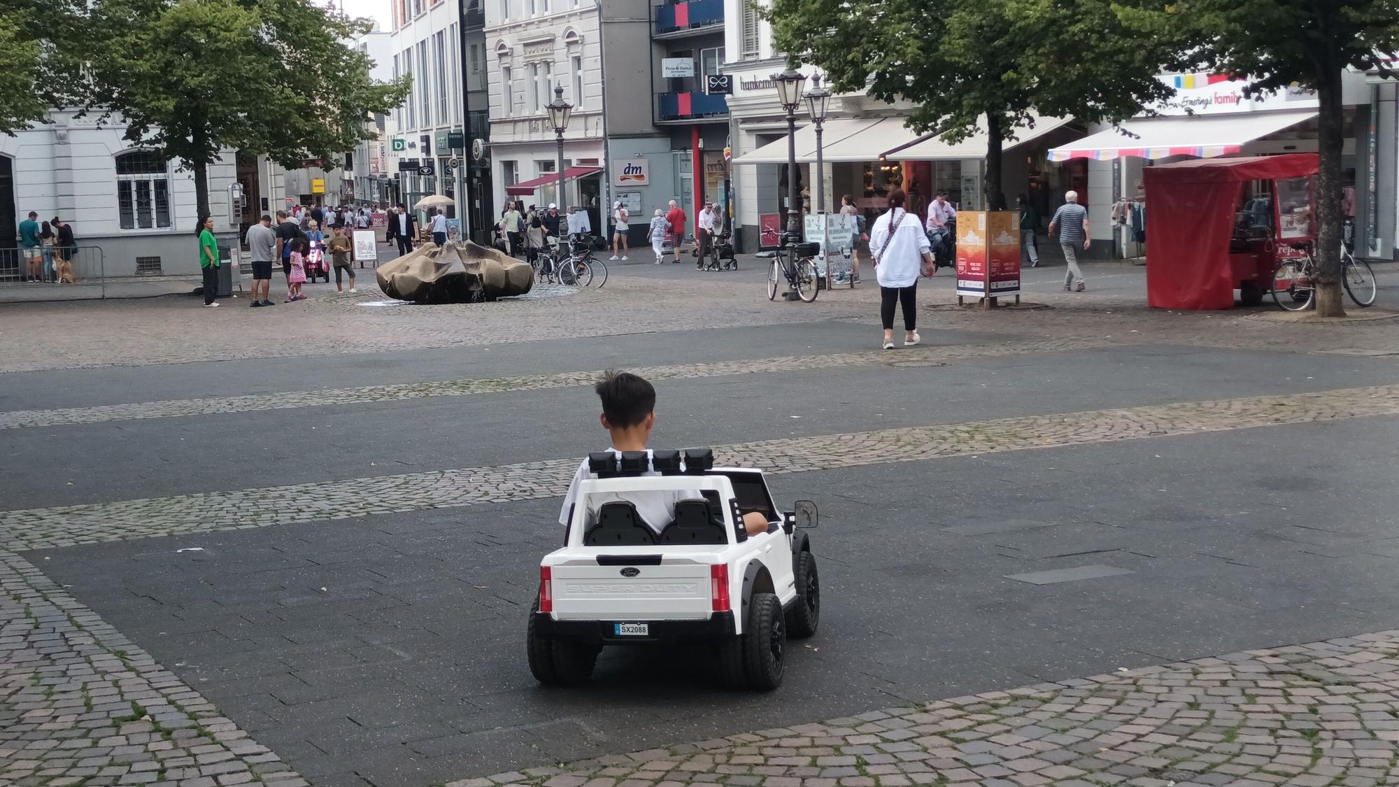 Kind in einem Elektro-Auto auf einem Platz in der Innenstadt