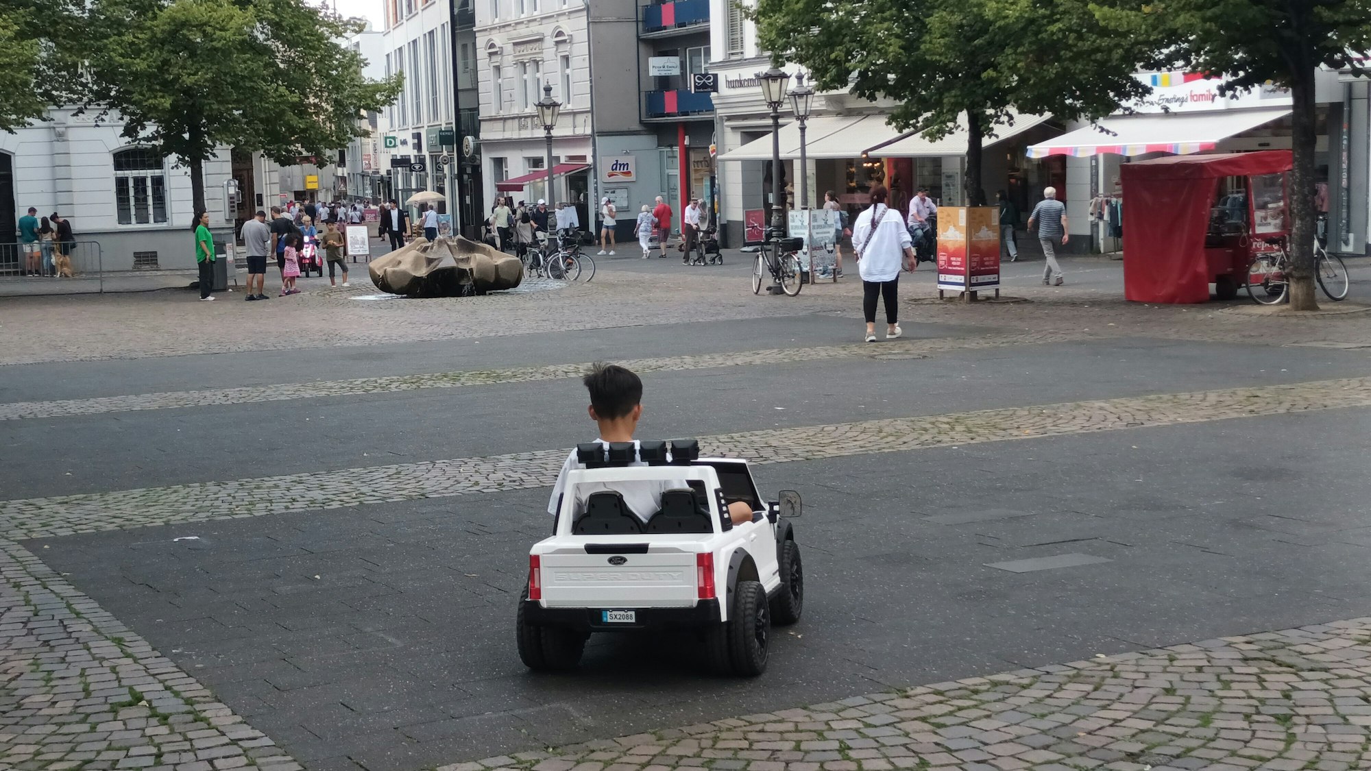 Kind in einem Elektro-Auto auf einem Platz in der Innenstadt