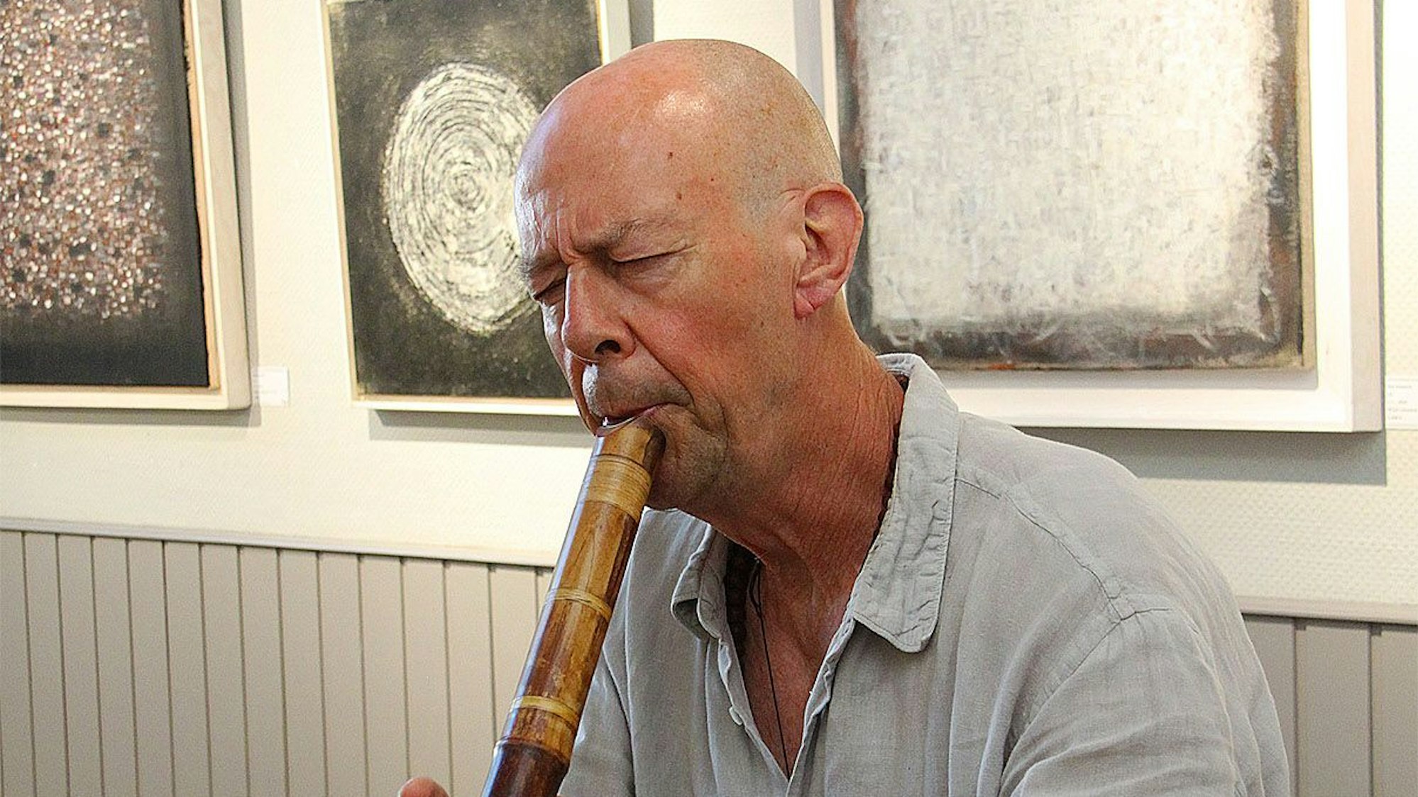 Dan Hepperle steht vor drei Kunstwerken und spielte auf einer japanischen Shakuhashi-Flöte.