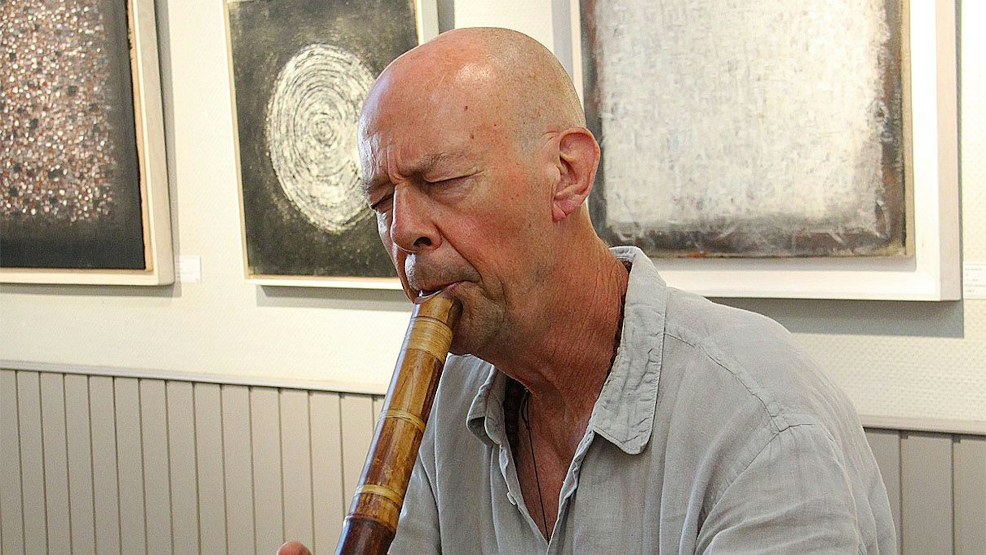 Dan Hepperle steht vor drei Kunstwerken und spielte auf einer japanischen Shakuhashi-Flöte.