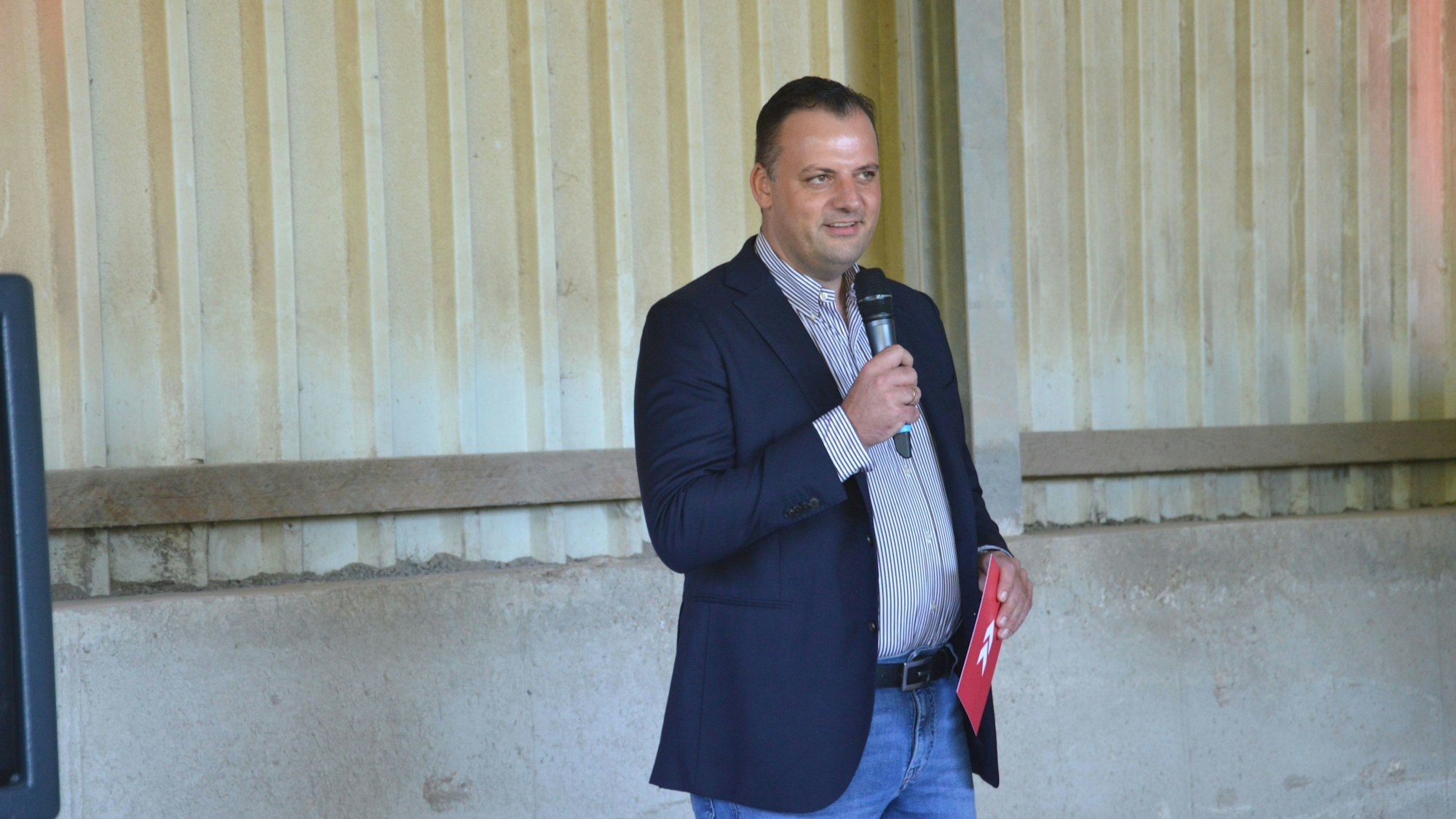 Marco Ilian, Gesellschafter der IK Umwelt Gruppe, steht mit einem Mikro in der Hand vor den Gästen.