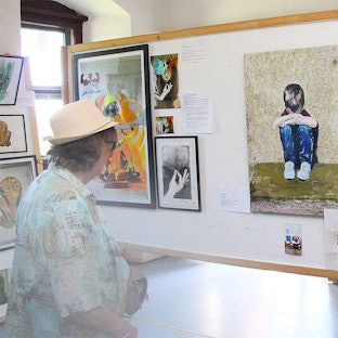 Eine Frau und ein Mann tragen Sommerhüte. Sie sind von hinten zu sehen, wie sie in einem Haus in Dahlem-Kronenburg Kunstwerke betrachten.