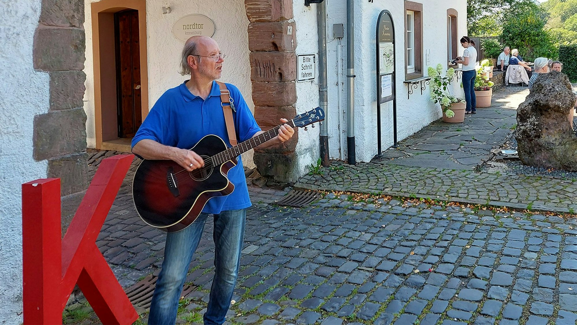 Der Musiker Tom Dolan steht vor dem Nordtor in Dahlem-Kronenburg und spielt auf einer Gitarre.