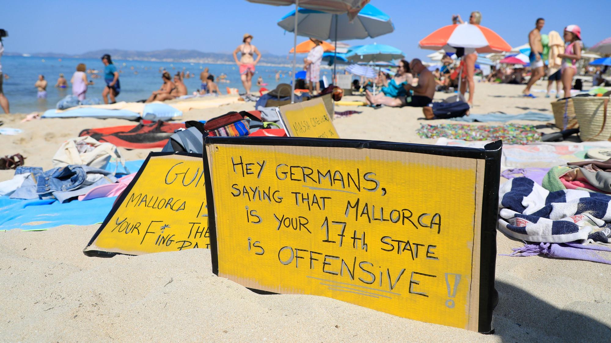 El Arenal: ‚Hallo Deutsche, zu sagen, dass Mallorca euer 17. Bundesland ist, ist offensiv-aggressiv‘ steht auf einem Schild, das an einem Strand auf Mallorca aus Protest gegen den Massentourismus auf der Balearen-Insel gezeigt wird.