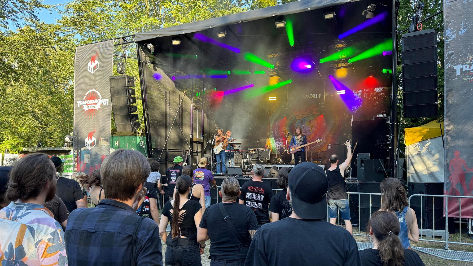 Rockfans feiern vor der bunt beleuchteten Open-Air-Bühne, auf der die Band Wight rockt.