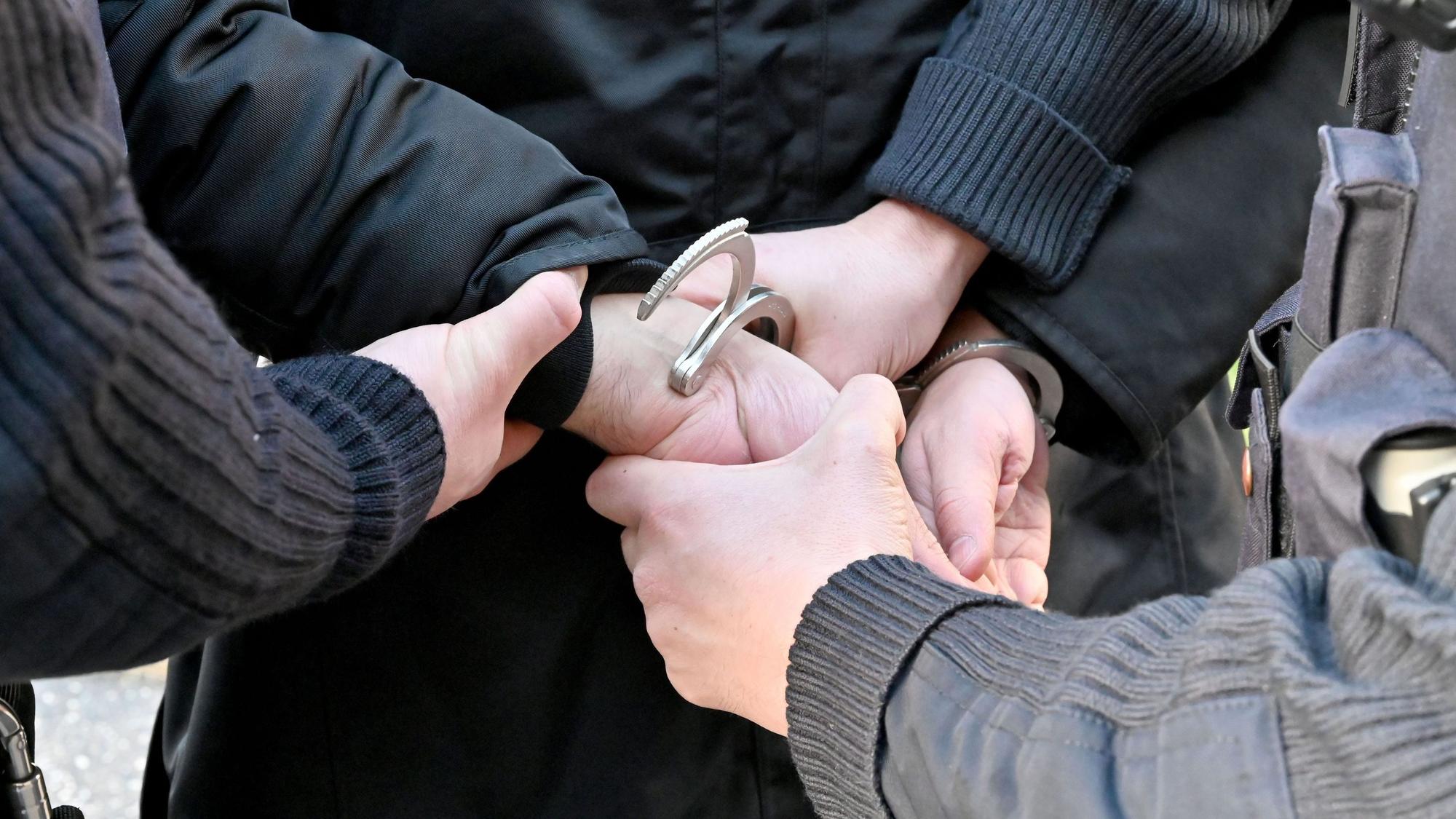 Das Symbolbild zeigt, wie Polizeibeamte einem Mann Handfesseln anlegen (Detailaufnahme).