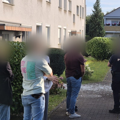 12.08.2024, Nordrhein-Westfalen, Köln: Einsatzkräfte stehen nach einer Explosion an einem Mehrfamilienhaus im Stadtteil Zündorf.