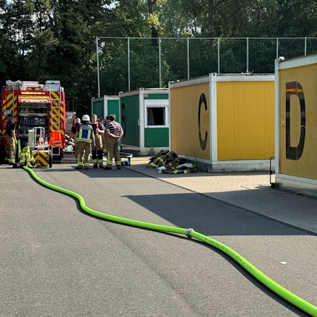 Das Bild zeigt Feuerwehrleute im Einsatz an einem Containerdorf.