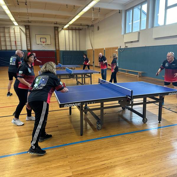 Mehrere Leute spielen in einer Sporthalle an mehreren Platten Tischtennis.