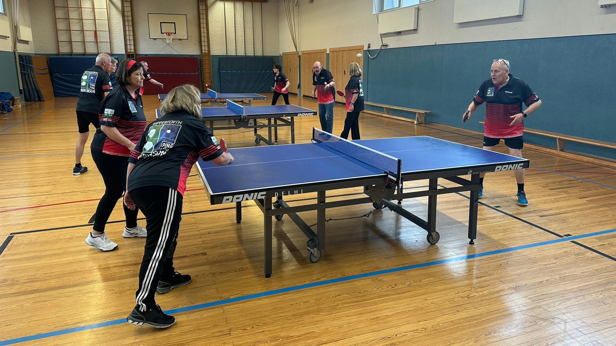 Mehrere Leute spielen in einer Sporthalle an mehreren Platten Tischtennis.