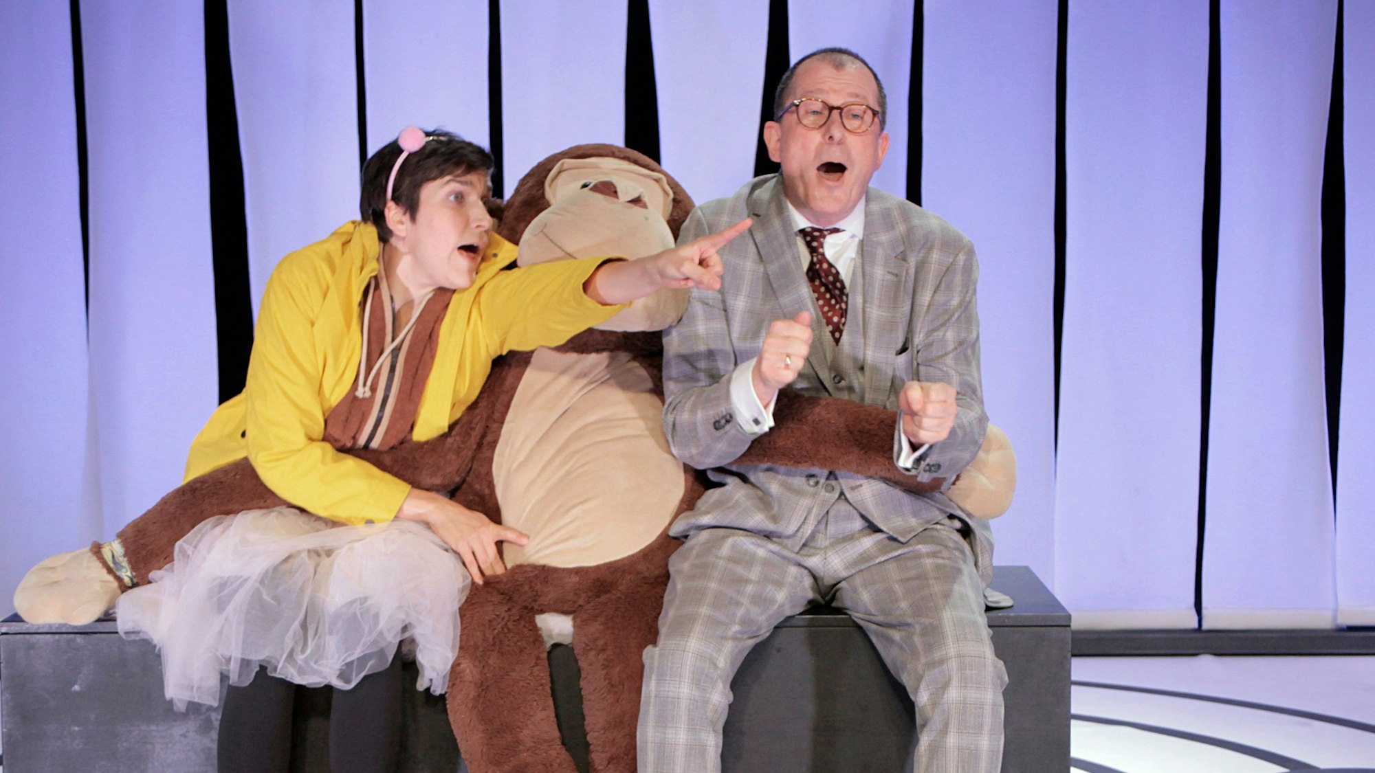 Auf dem Foto sind zwei Schauspieler mit einem großen Plüschaffen zu sehen.