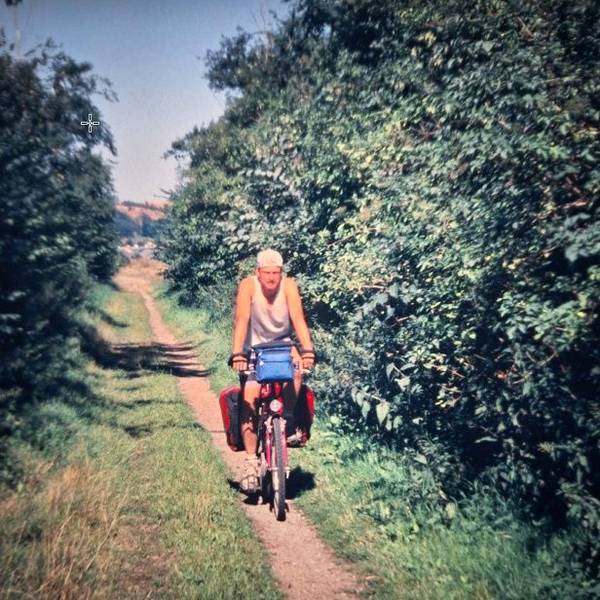Ein Mann fährt auf einem Fahrrad auf einem schmalen Pfad zwischen Bäumen hindurch.