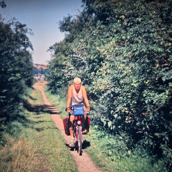Ein Mann fährt auf einem Fahrrad auf einem schmalen Pfad zwischen Bäumen hindurch.
