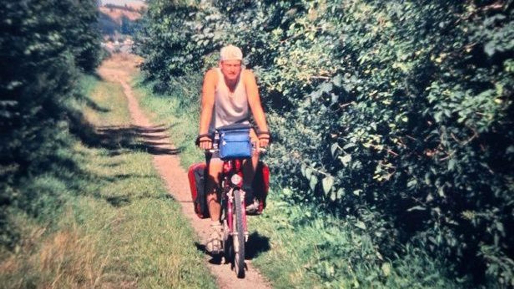 Ein Mann fährt auf einem Fahrrad auf einem schmalen Pfad zwischen Bäumen hindurch.