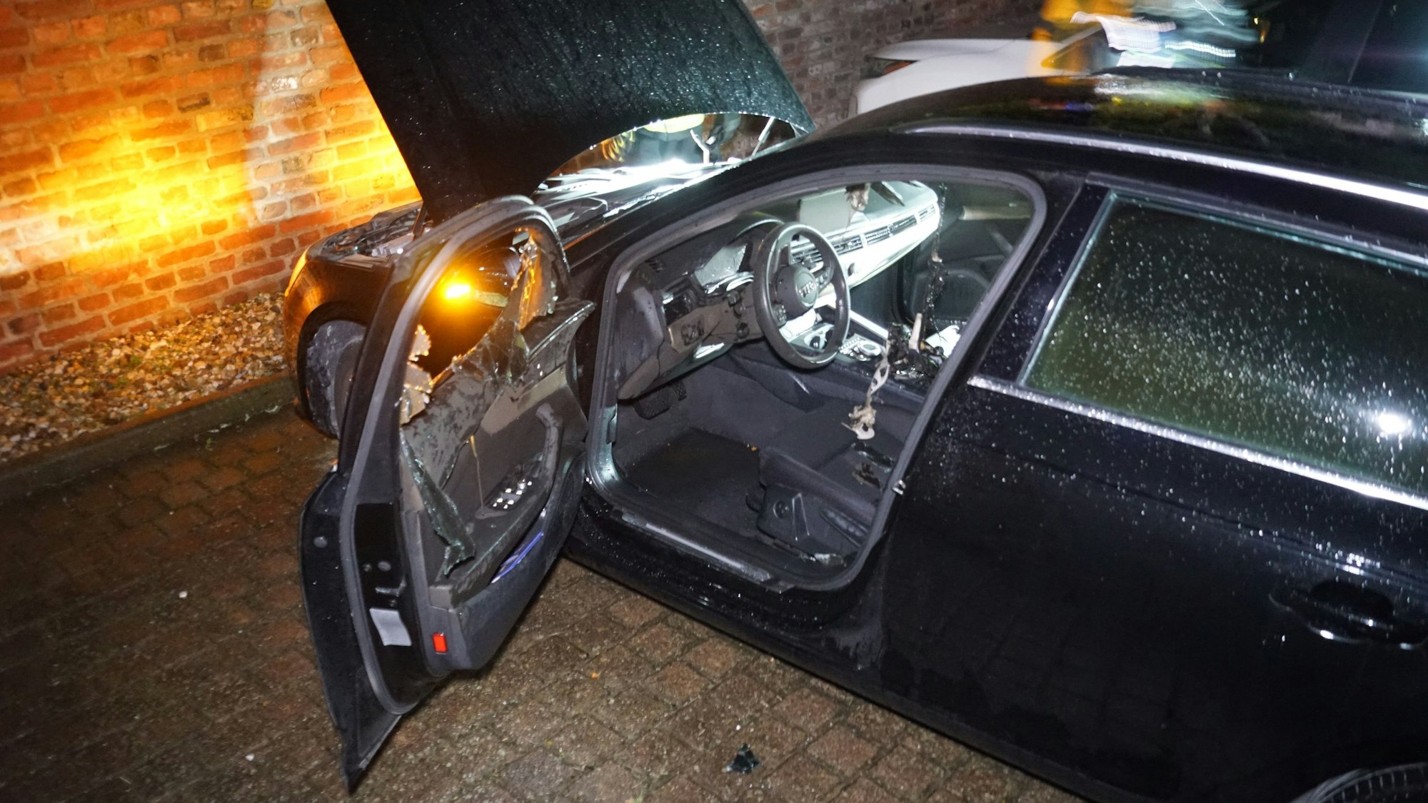 Ein Auto steht mit offener Tür vor einer Wand, der Innenraum ist beschädigt.