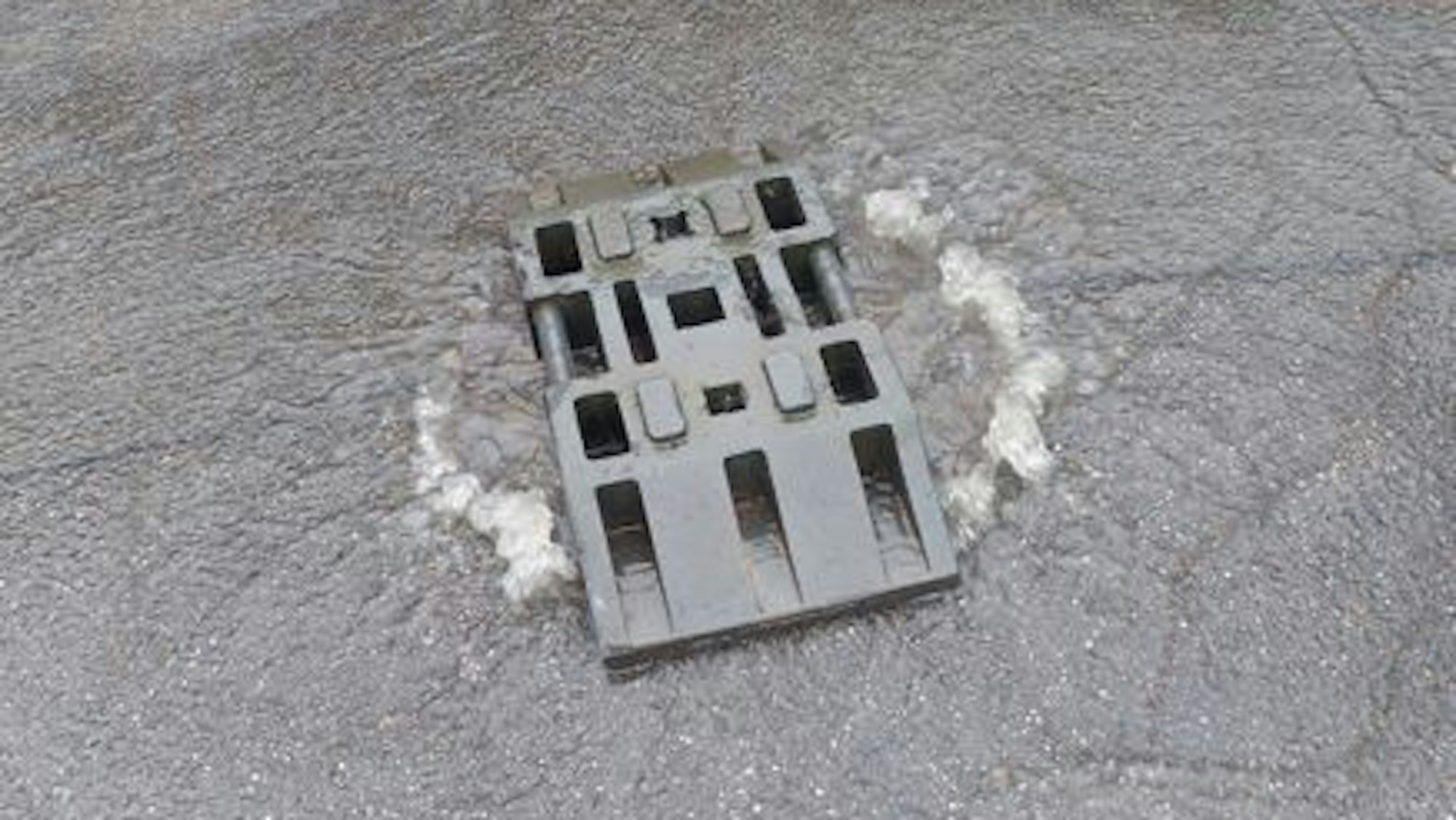 Auf einem überlaufenden Gully liegt ein Baustein.