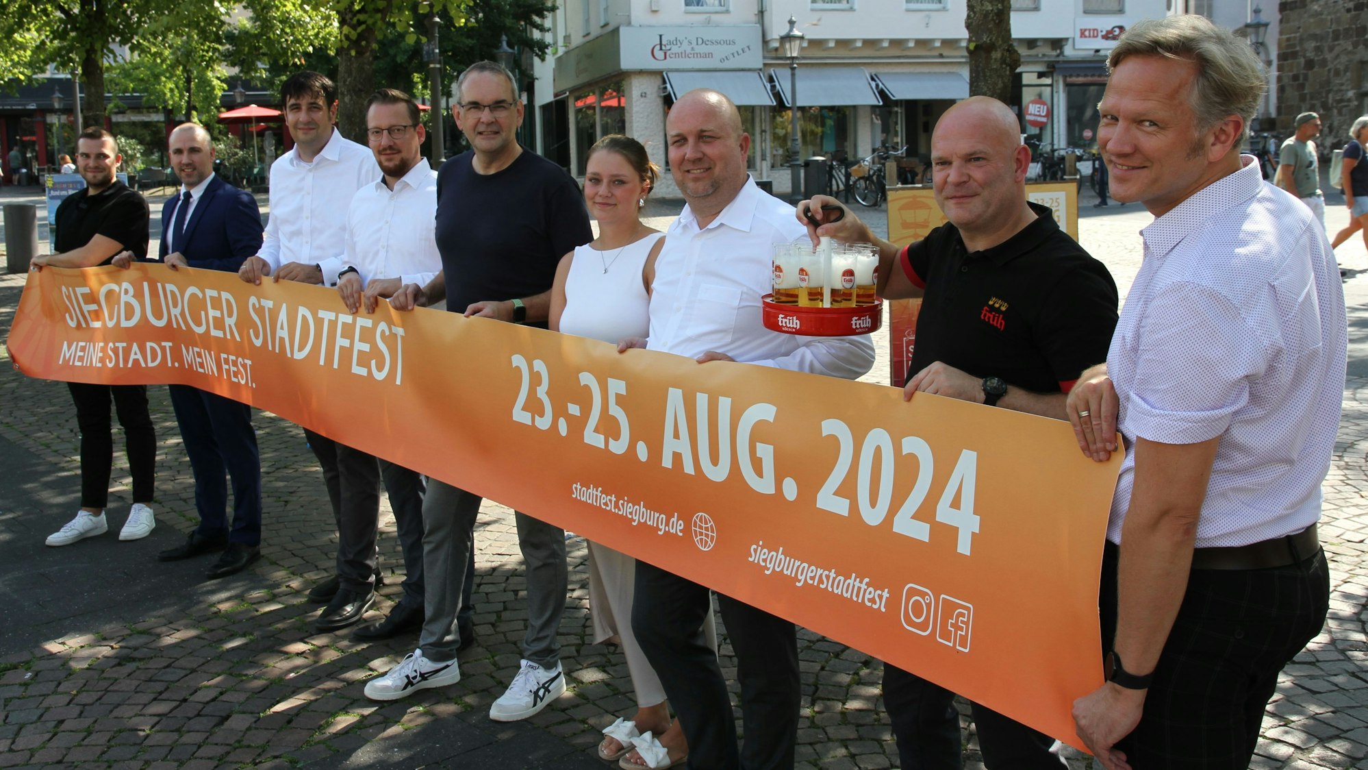 Neun Männer und eine Frau halten ein orangefarbenes Werbebanner für das Siegburger Stadtfest
