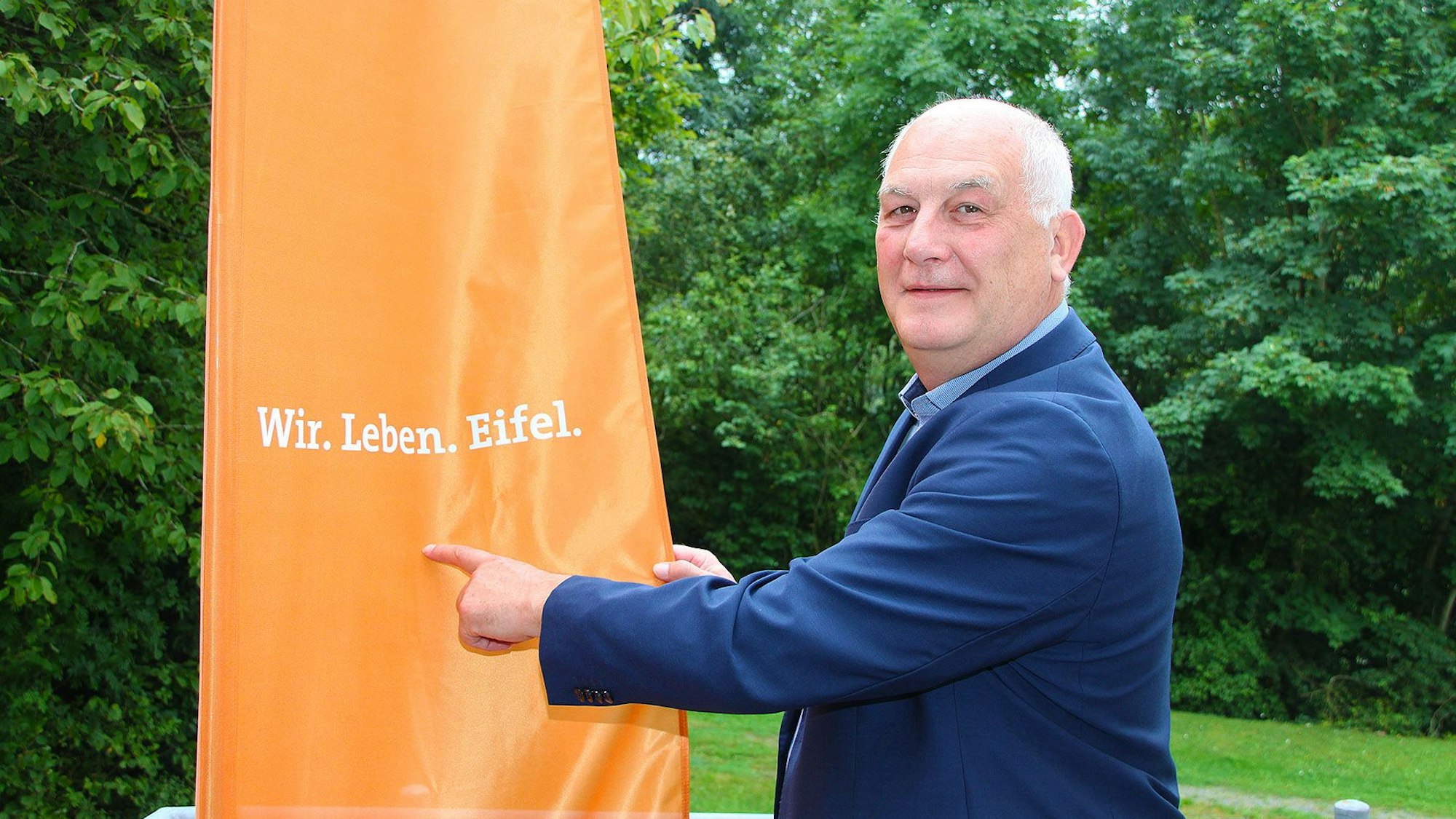 Klaus Schäfer zeigt auf den Slogan „Wir. Leben. Eifel“.