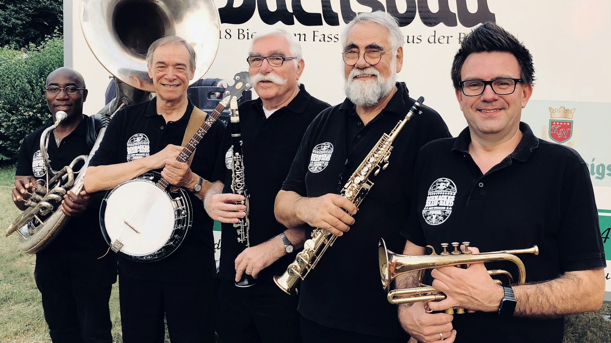 Fünf Musiker, bekleidet mit schwarzen T-Shirts, lächeln in die Kamera.