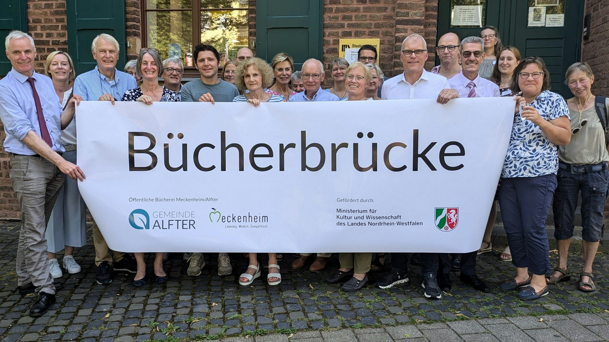 Alle Akteure der Öffentlichen Bücherei Meckenheim-Alfter zeigen ein Plakat mit dem neuen Namen Bücherbrücke.