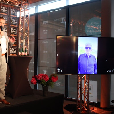 Marc Brucherseifer steht auf der Bühne und spricht in ein Mikrofon. Auf einem Bildschirm ist Heino zu erkennen.