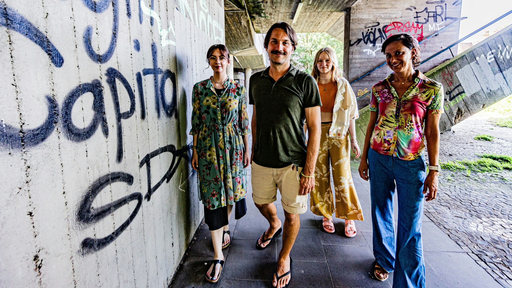 Vier Menschen vor einer Wand mit Graffiti.
