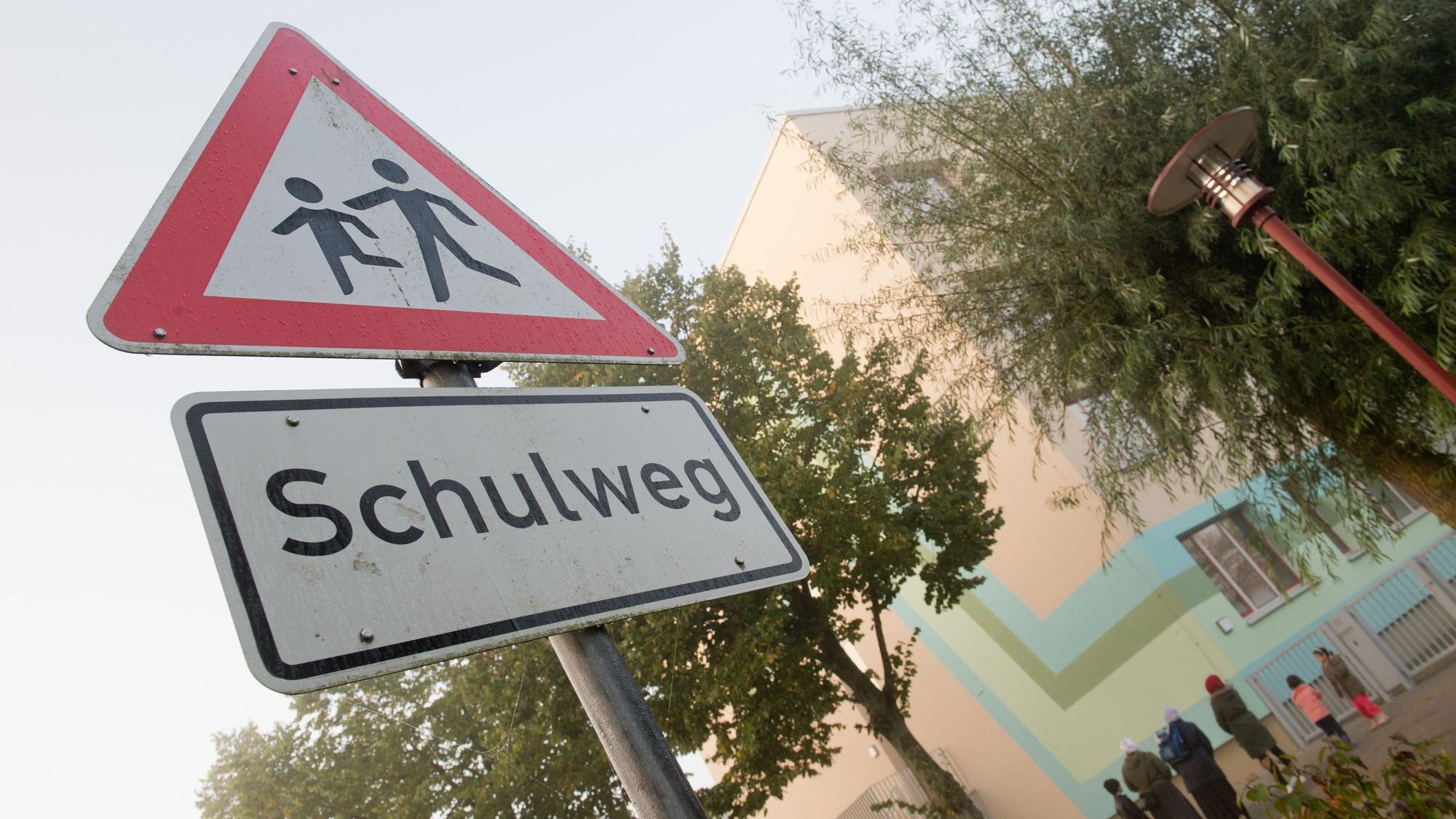 Ein Warnschild "Schulweg" steht vor einer Schule.
