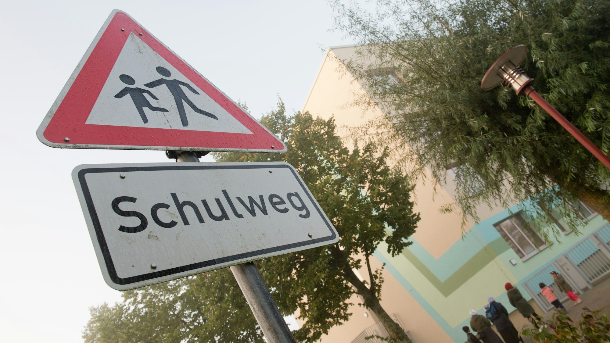 Ein Warnschild "Schulweg" steht vor einer Schule.