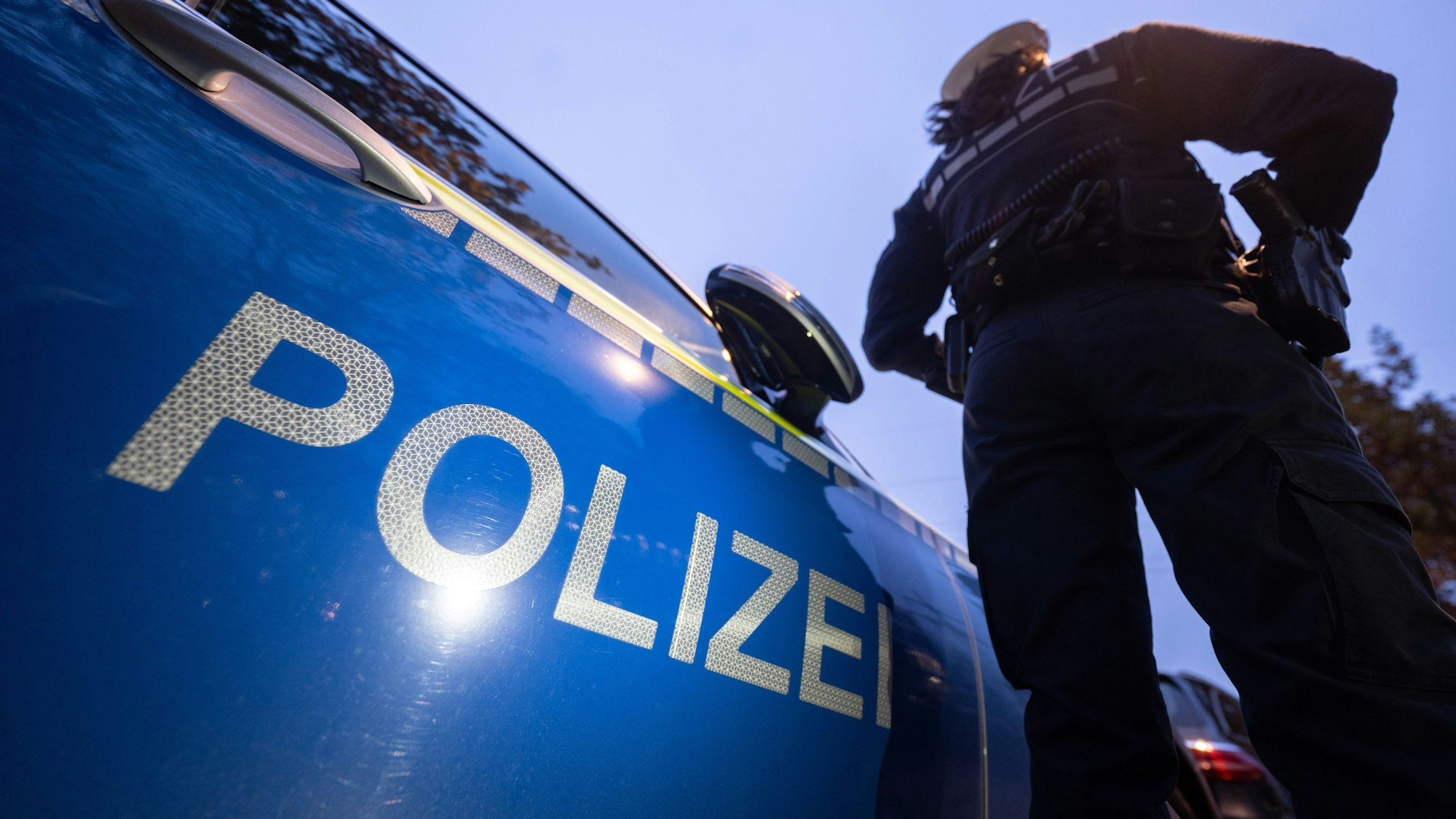 Eine Polizistin steht neben einem Polizeifahrzeug.