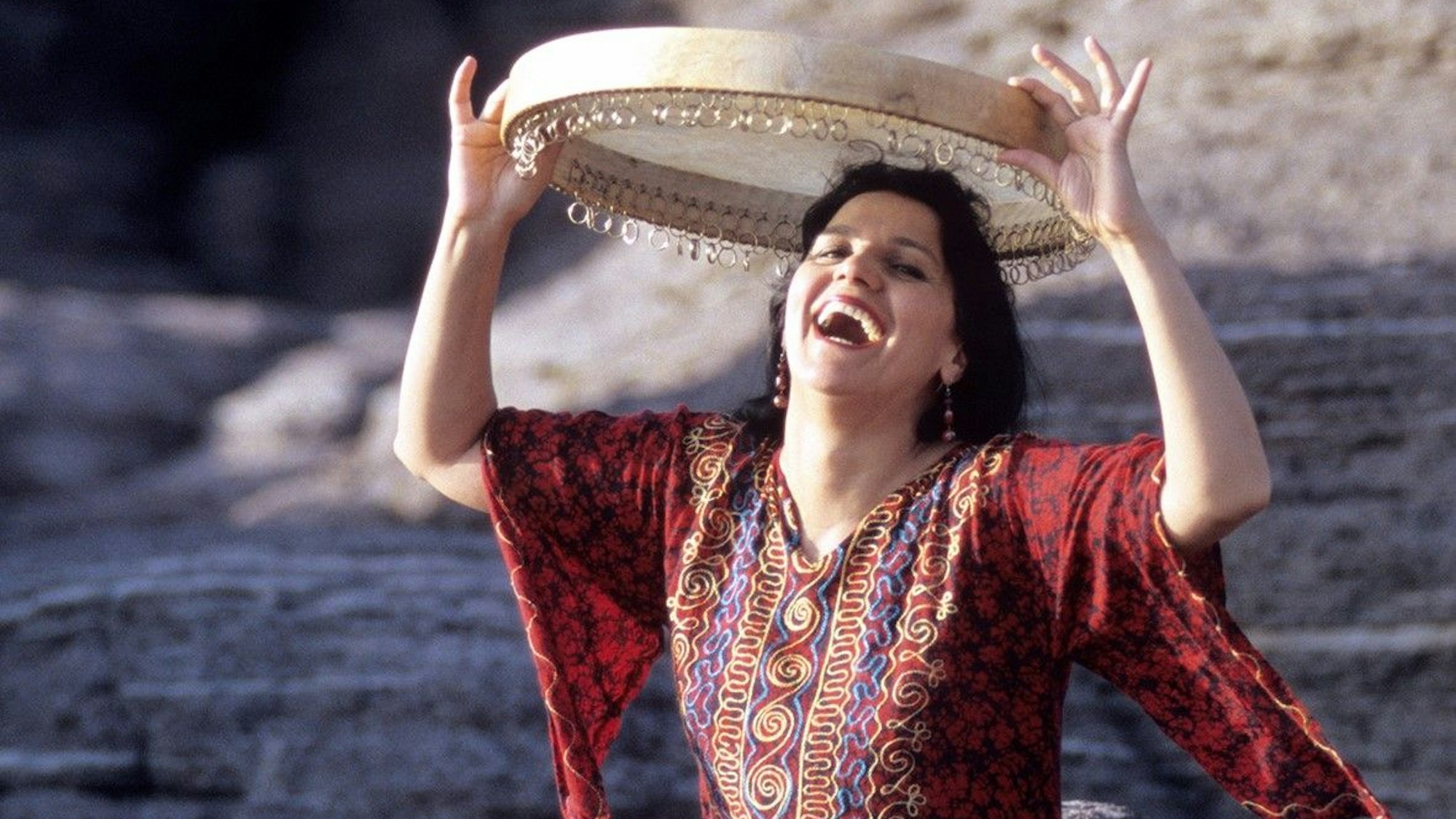 Eine lachende Frau, über ihrem Kopf hält sie ein Tamburin.