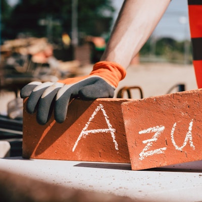 Das Bild zeigt zwei Hände, die zwei Ziegelsteine halten, auf denen das Wort Azubi steht.