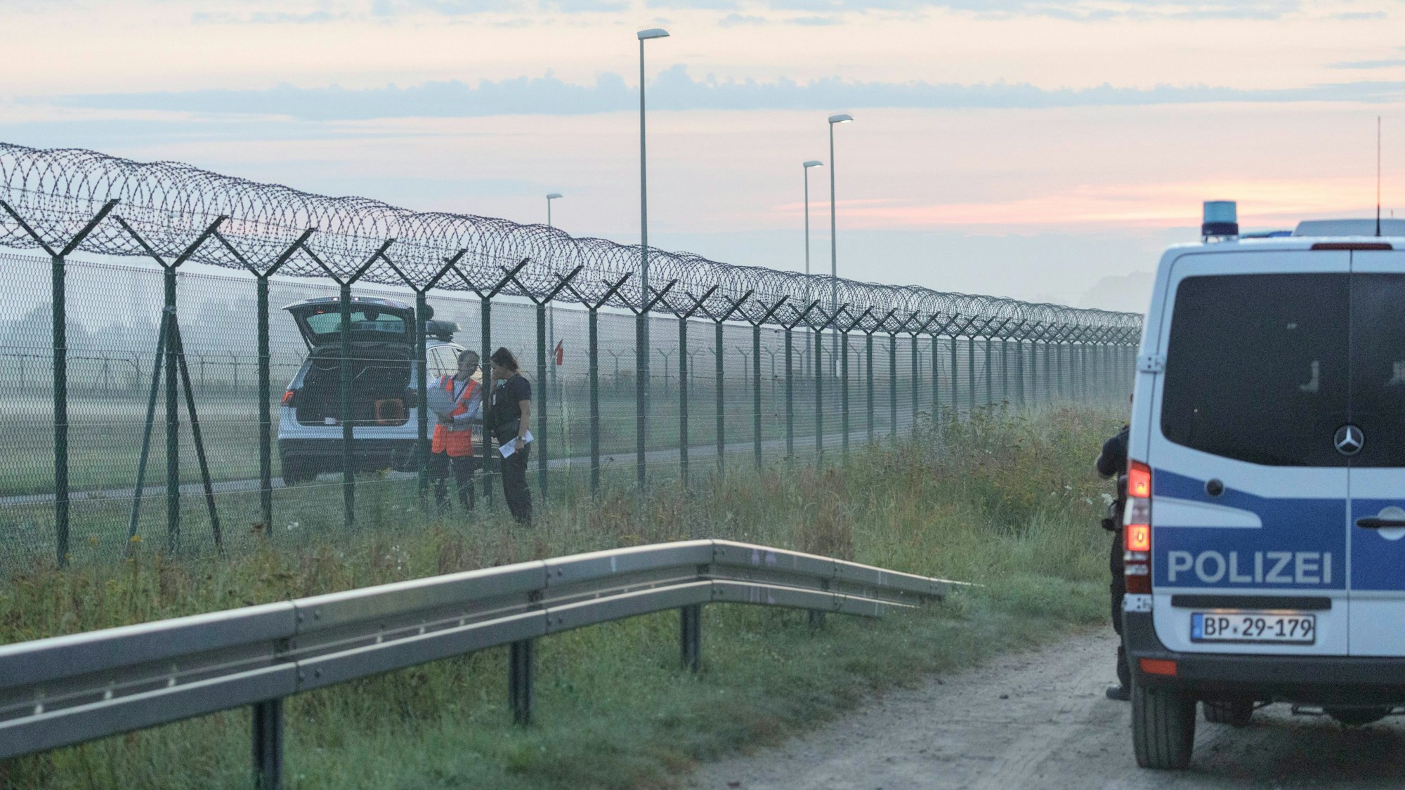 Eine Mitarbeiterin der Flughafensicherheit des Flughafen Berlin-Brandenburg BER spricht mit einer Bundespolizistin am Zaun des Flughafens.