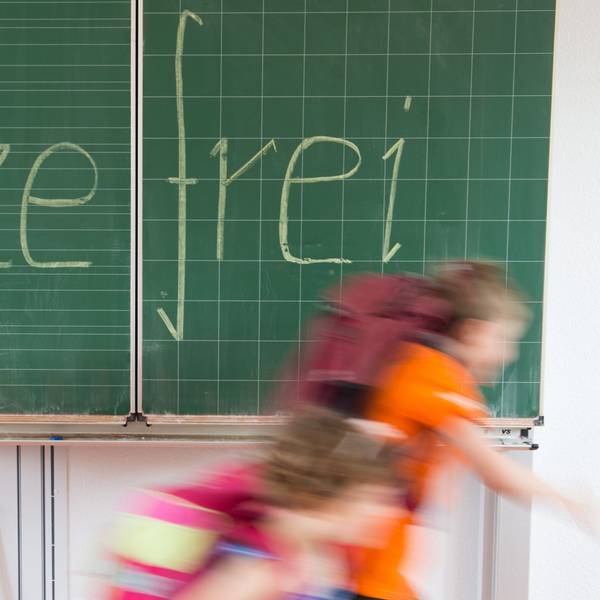 Grundschüler verlassen den Klassenraum. Hinter ihnen ist mit Kreide das Wort „Hitzefrei “an die Tafel geschrieben. (Symbolbild)
