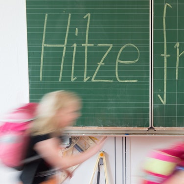 Grundschüler verlassen den Klassenraum. Hinter ihnen ist mit Kreide das Wort „Hitzefrei “an die Tafel geschrieben. (Symbolbild)
