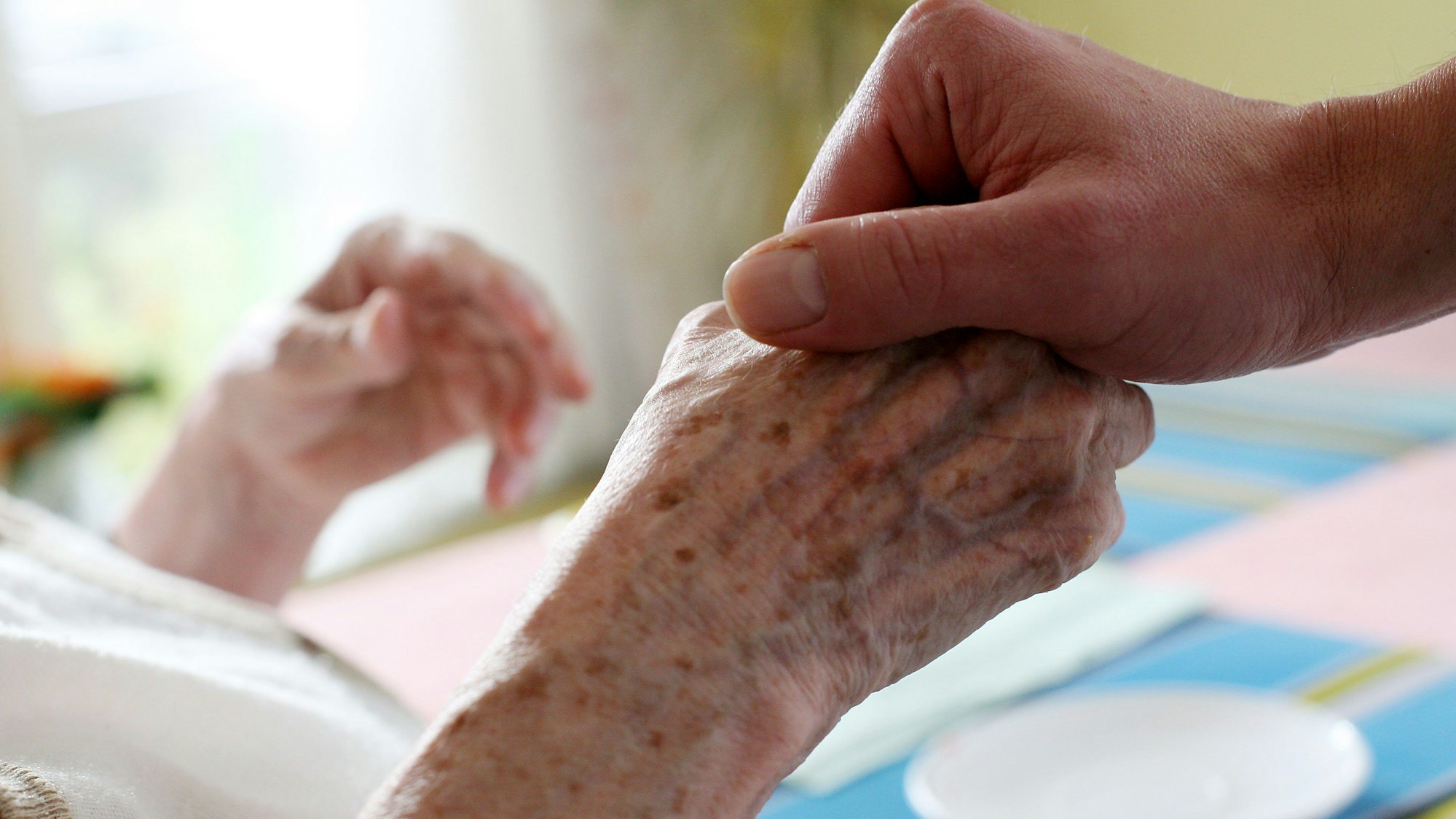 Eine Hand hält die Hand einer Seniorin in einer Pflegeeinrichtung.