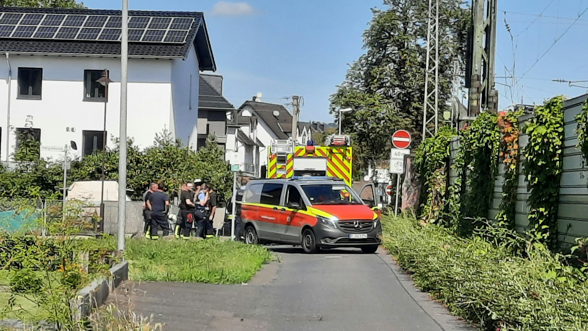 Feuerwehrleute und -fahrzeuge stehen in einer Straße neben Bahngleisen.