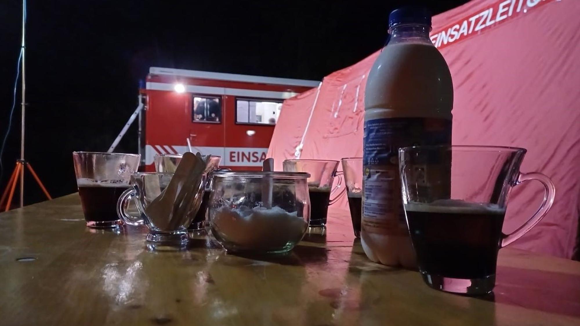 Einige Kaffeegläser stehen auf einem Tisch. Im Hintergrund ist ein Einsatzleitwagen der Feuerwehr zu erkennen.