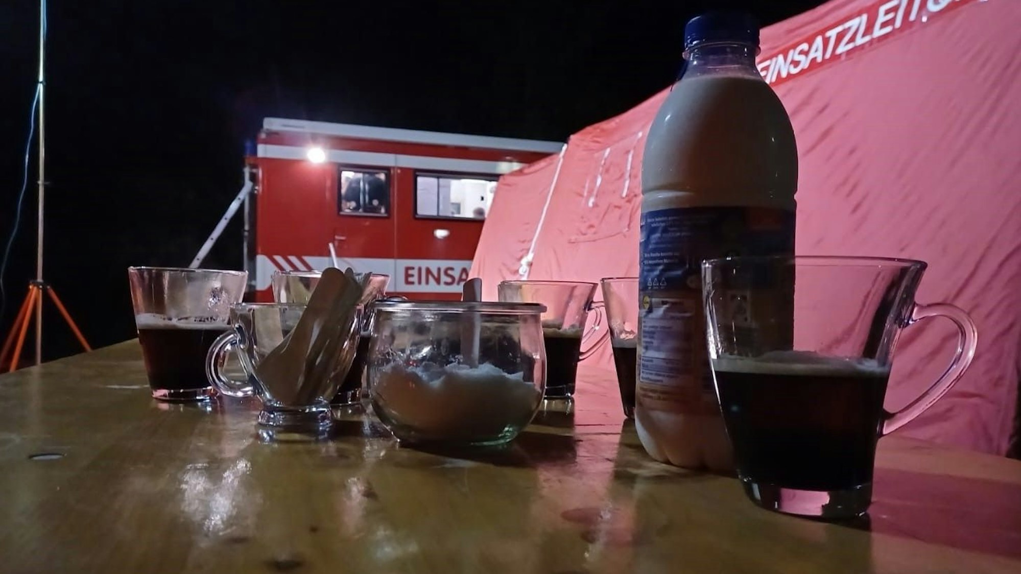 Einige Kaffeegläser stehen auf einem Tisch. Im Hintergrund ist ein Einsatzleitwagen der Feuerwehr zu erkennen.