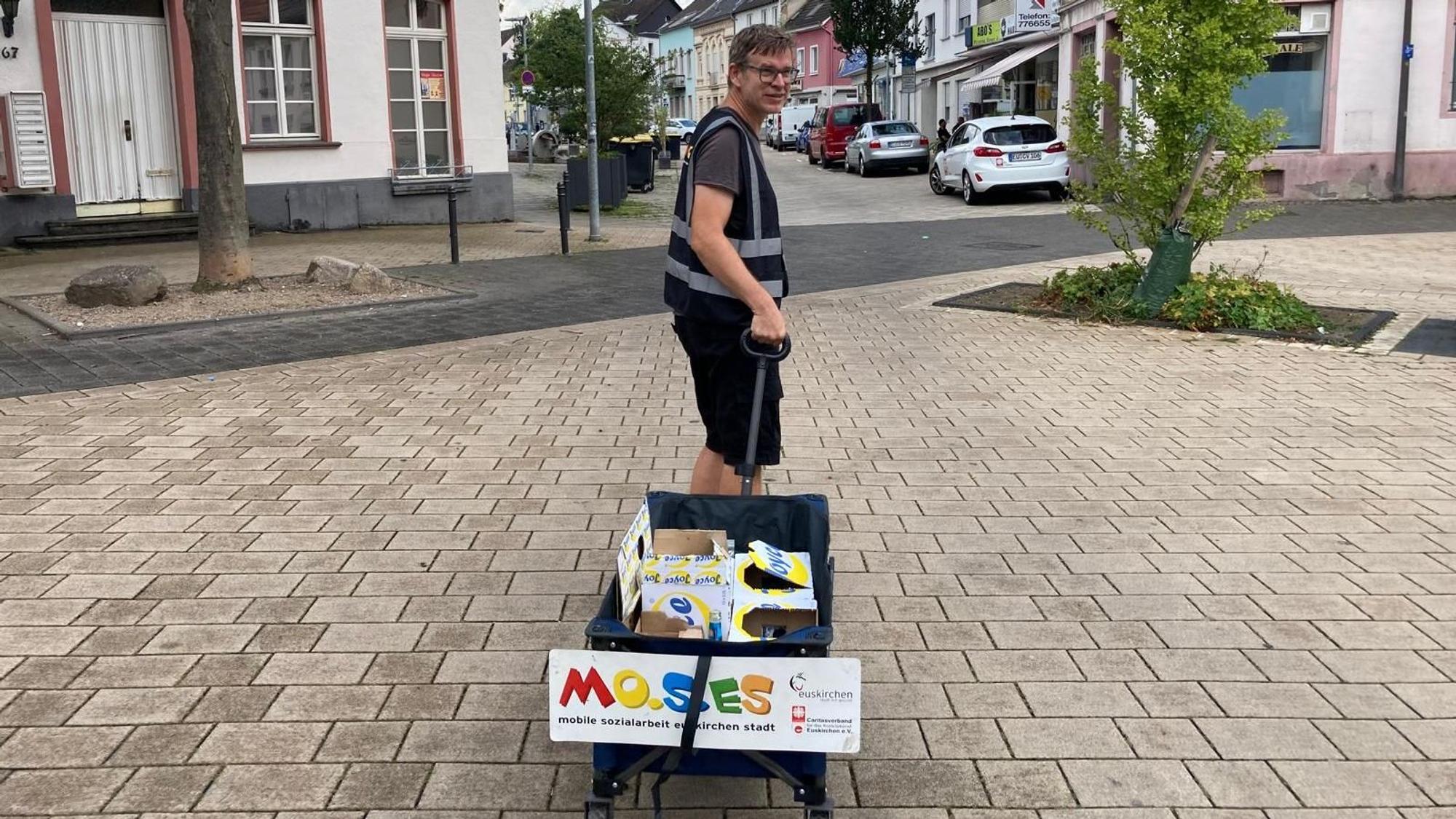 Ein Mann zieht einen Bollerwagen durch eine Innenstadt.